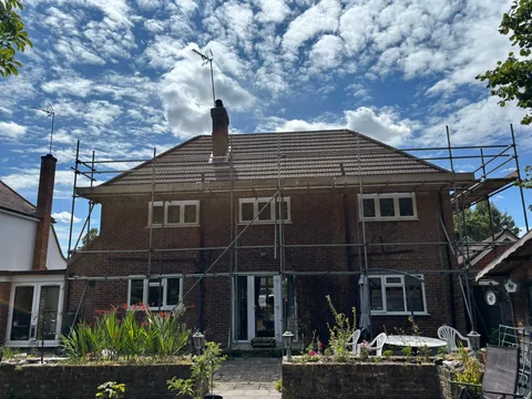 Scaffold up all round a brick house with a brown tile roof and chimney stack